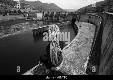 Young woman sitting near an old hydroelectric plant. Black-and-white photo. Stock Photo