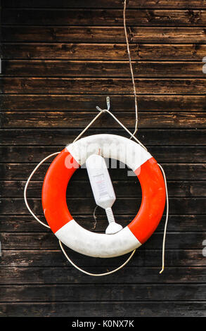 Red and white lifebuoy lifebelt with ropes hanging from a dark brown painted wooden wall. Portrait orientation. Stock Photo