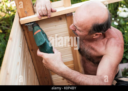 Mature man using power drill building something at contryhouse Stock Photo