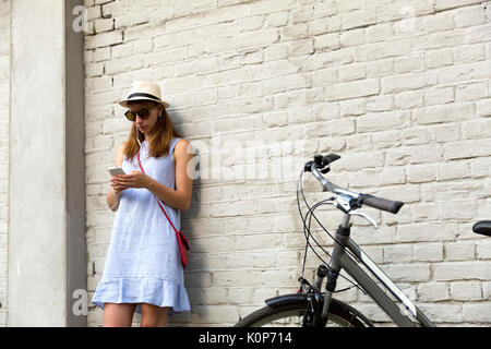 City life concept. Young woman standing next to the white brick wall listening to music in headphones Stock Photo