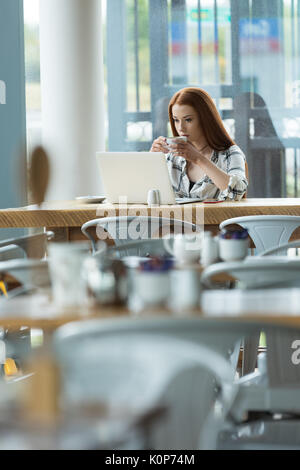 Woman having coffee while using laptop computer at table in cafe Stock Photo