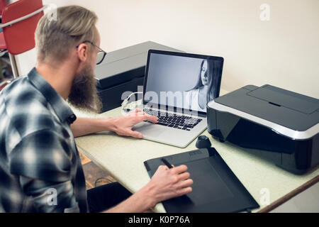 Photographer using graphics tablet while editing while sitting at table n studio Stock Photo