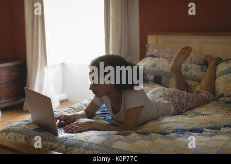 Woman lying and using laptop on bed in bedroom Stock Photo