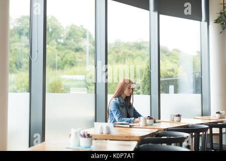 Young woman sitting at table by window in cafe Stock Photo