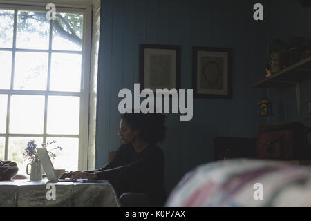 Beautiful woman using laptop while sitting on chair in living room Stock Photo
