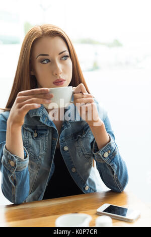 Thoughtful young woman holding coffee cup by window in cafe Stock Photo