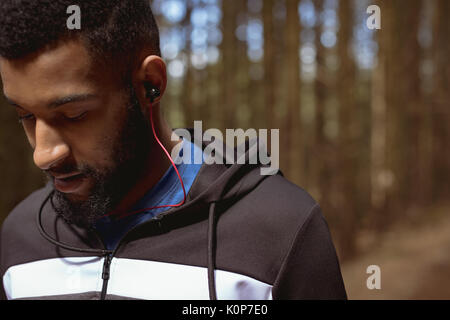 Close up of young man listening music while standing in forest Stock Photo