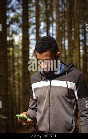 Young man using cell phone while standing in forest Stock Photo