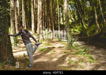 Full length of young man exercising by tree in forest Stock Photo