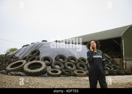 Female farmer talking on mobile phone near farm in field Stock Photo