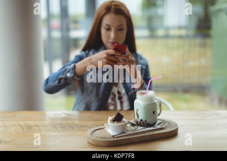 Woman photographing drink and dessert on tray at table while sitting in cafe Stock Photo