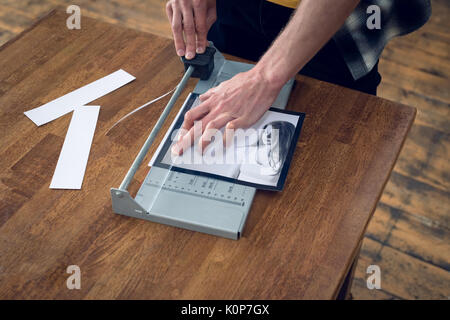 High angle view of photographer cutting photograph with tool at table in studio Stock Photo