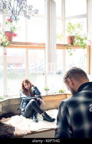 Man photographing female fashion model sitting on alcove window seat in studio Stock Photo