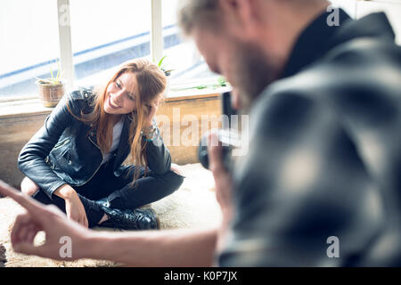 Close up of Photographer photographing fashion model sitting on alcove window seat in studio Stock Photo