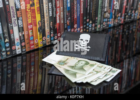 Stacked DVD movies & black pirate wallet and Chinese renminbi banknotes. Metaphor Chinese copyright IP theft, US-China trade war, China piracy. Stock Photo