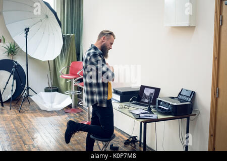 Side view of photographer looking at photographs at table in studio Stock Photo