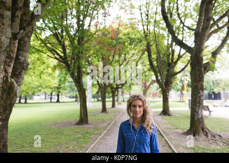 Portrait of young woman standing on footpath amidst trees at park Stock Photo