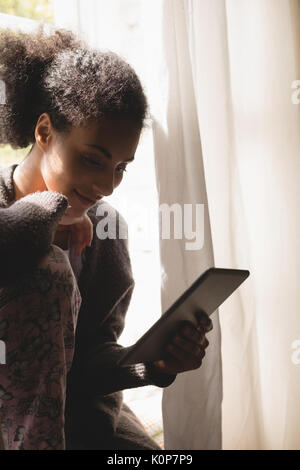 Woman using digital tablet while sitting at window sill at home Stock Photo