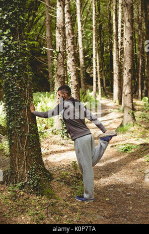 Full length of man exercising by tree in forest Stock Photo