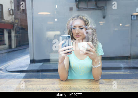 young woman using phone seen through glass at cafe Stock Photo