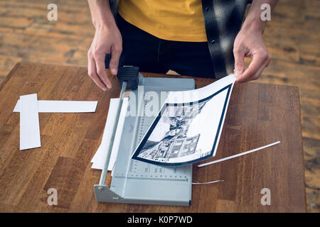 Mid section of photographer cutting photograph on paper cutting tool at table in studio Stock Photo