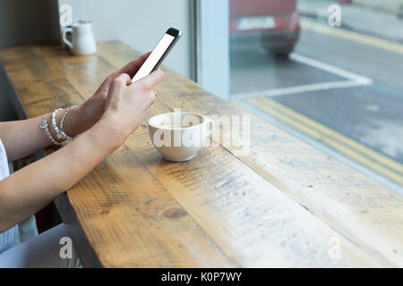 Cropped image of young woman using phone while sitting at tabke in cafe Stock Photo