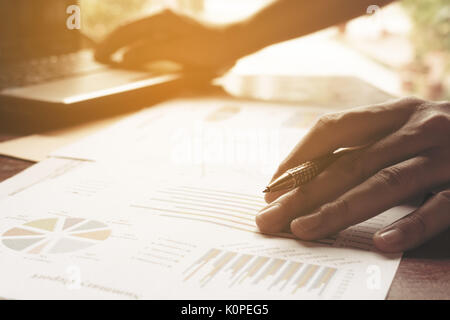 Young businessman holding pen on charts and graph to find out the result at home office. Stock Photo