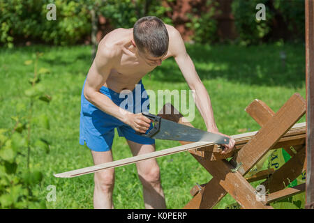 A young man holding a hand saw saws a board Stock Photo