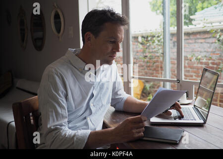 Man using laptop and reading document in home office Stock Photo