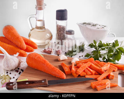 Carrots chopped on chopsticks surrounded by greenery, parsley, dill, garlic, pepper, vegetable oil in a bottle with a stopper, pepper and salt in jars Stock Photo