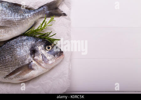 Fresh raw sea bream fish with lemon slices, salt, rosemary and olive oil on white wooden table.Healthy food concept, top view, copy space Stock Photo