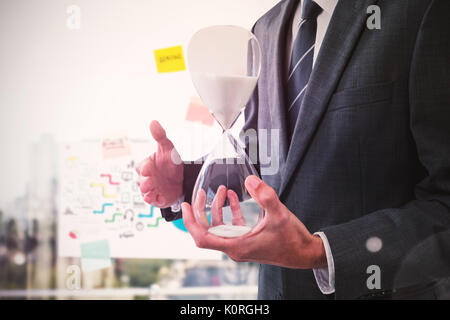 Mid section of businessman holding hourglass against adhesive notes on window Stock Photo