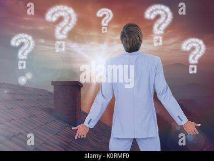 Digital composite of Question marks and Businessman standing on Roof with chimney and epic twilight sunset Stock Photo
