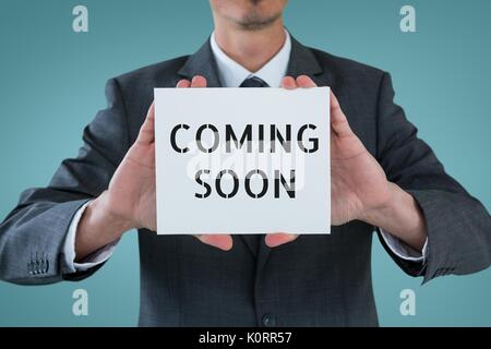 Digital composite of Business man holding a card with coming soon text Stock Photo