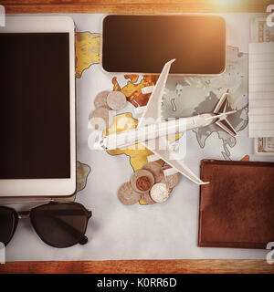 Overhead view of toy airplane by passport and currency with technologies on map at table Stock Photo