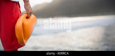 Cropped image of man holding rescue buoy against mountain against sky at beach Stock Photo