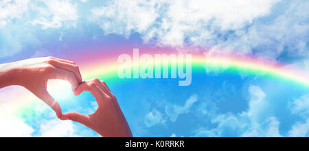 Hands making heart shape on the beach against clouds against blue sky Stock Photo