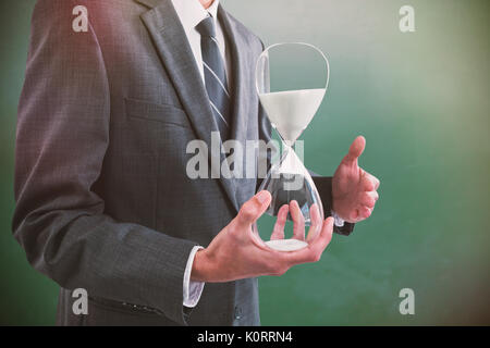 Mid section of businessman holding hourglass against green chalkboard Stock Photo