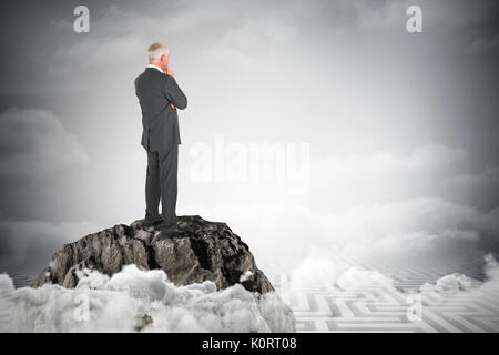 Thoughtful businessman standing back to camera against maze ending in cloudy sky Stock Photo