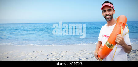 Portrait of male lifeguard holding life belt against beach against clear sky Stock Photo