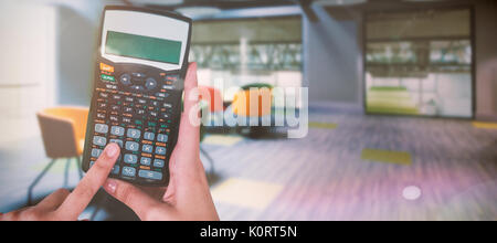 Hands of businesswoman using calculator against chairs on floor at modern building Stock Photo
