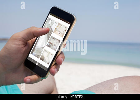 Interior of house on cellphone display against close up of man using smartphone at beach Stock Photo