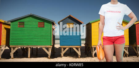 Mid section of female lifeguard holding rescue buoy against colorful huts on sand at beach Stock Photo