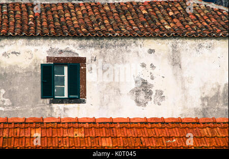 Detail from traditional old Portuguese facade with green and white wooden window, roof with old brown ceramic tiles and old and worn out wall backgrou Stock Photo