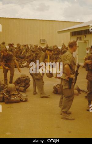 A large group of soldiers are gathered outside, in uniform with full combat gear, awaiting transportation, Bien Hoa Air Base, Vietnam, 1964. Stock Photo