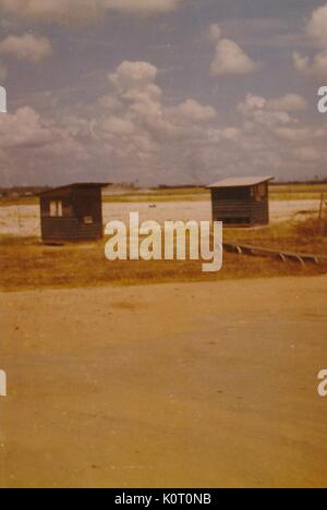 Two small, wooden structures can be seen at the air terminal, flat ground and low vegetation make up the background, Phu Bai Combat Base, Vietnam, 1964. Stock Photo