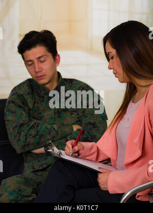 Handsome young soldier wearing uniform, with a woman therapist taking notes in a medical health center, in a office background Stock Photo