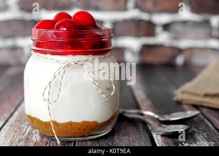Delicious cherry cheesecake in a mason jar on rustic wood with brick background