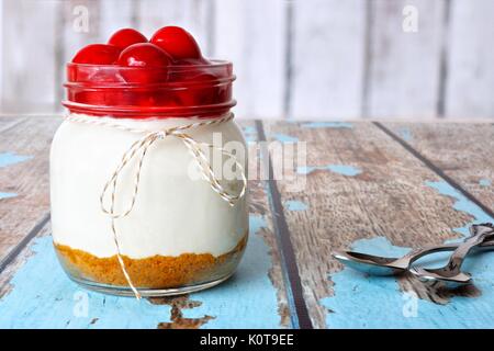 Sweet cherry cheesecake in a mason jar on a rustic wood background Stock Photo