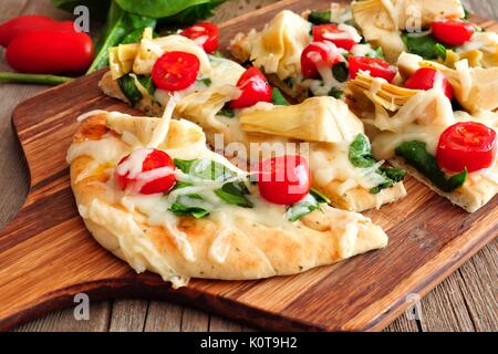 Healthy flat bread pizza with melted mozzarella, tomatoes, spinach and artichokes, close up on a paddle board Stock Photo